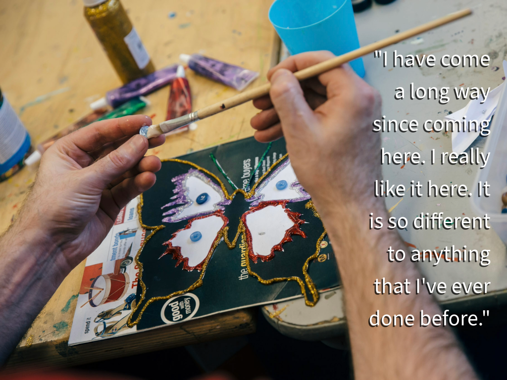 Hands holding a paint brush with an picture of a butterfly on the table in the background